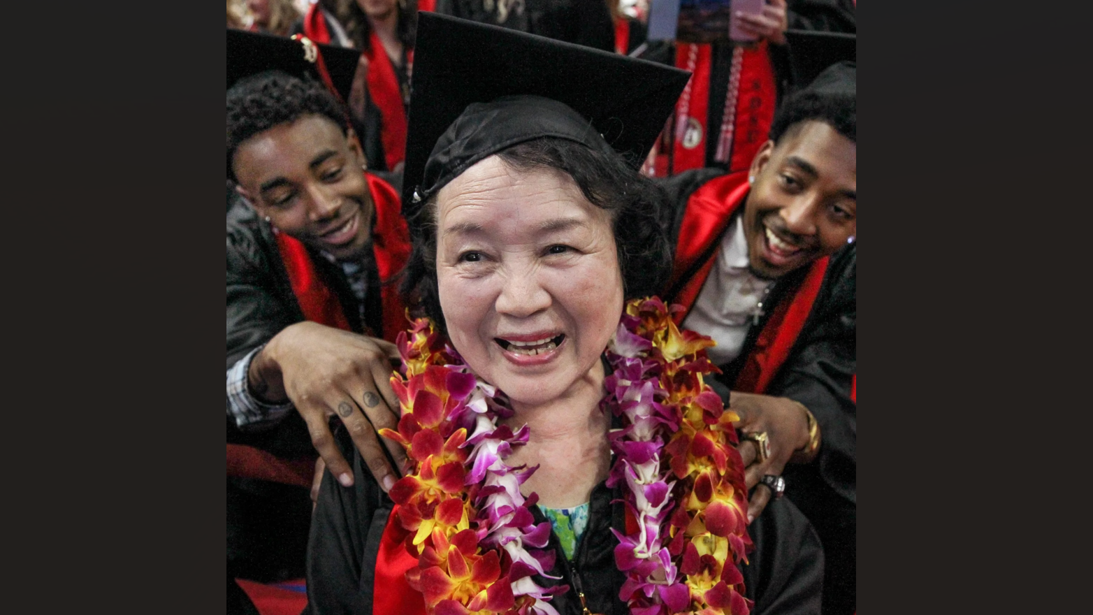 Elderly woman graduating with younger graduates congratulating her