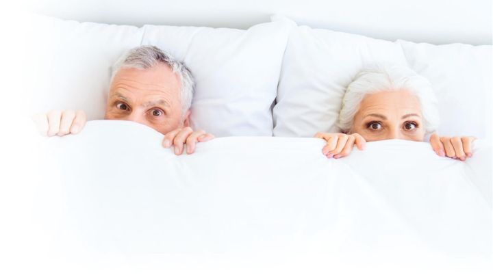 Mature couple with their heads peaking out of the blankets