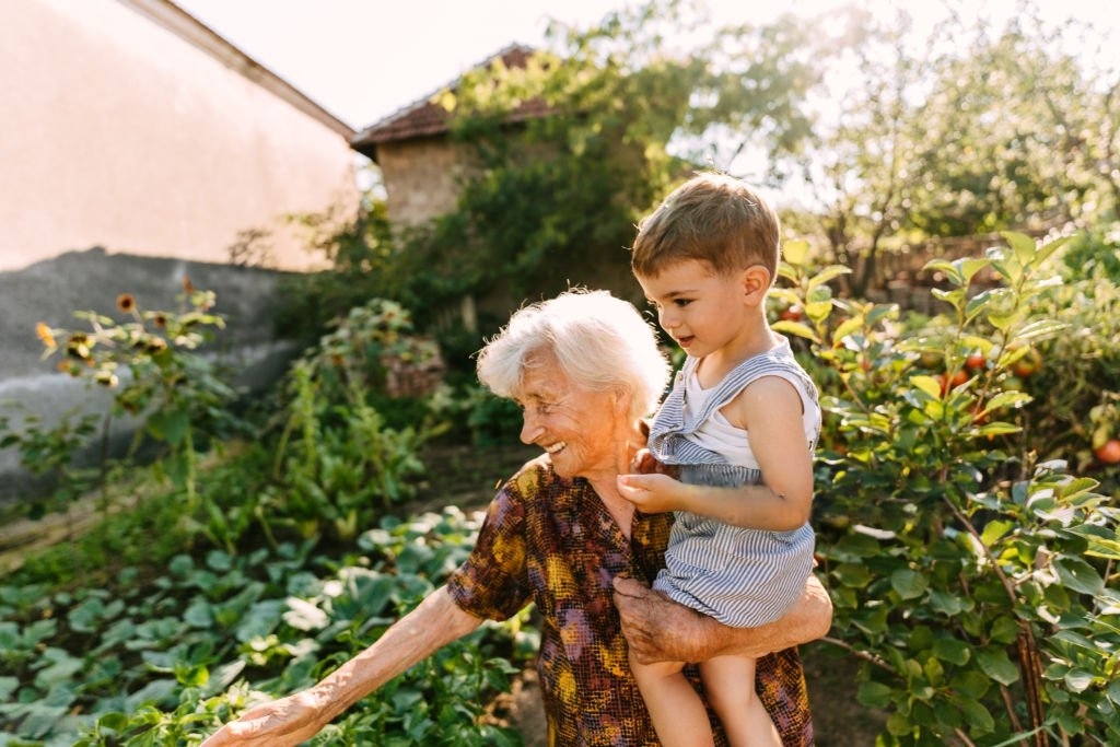 A grandmother holding up a young child while looking a plants
