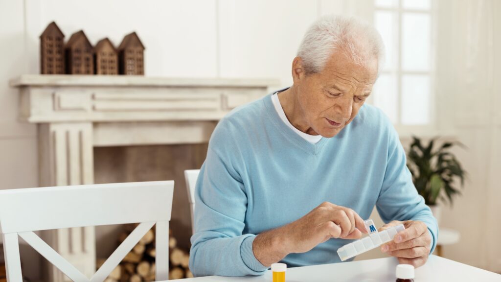 Elderly man sitting at the table and taking a pill while having his daily dose of medicine