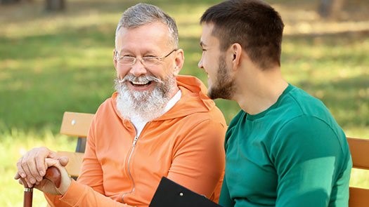 Male Caregiver sitting on park Bench with Senior male