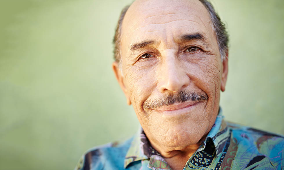 portrait of senior hispanic man with mustache looking at camera against green wall and smiling. Horizontal shape, copy space